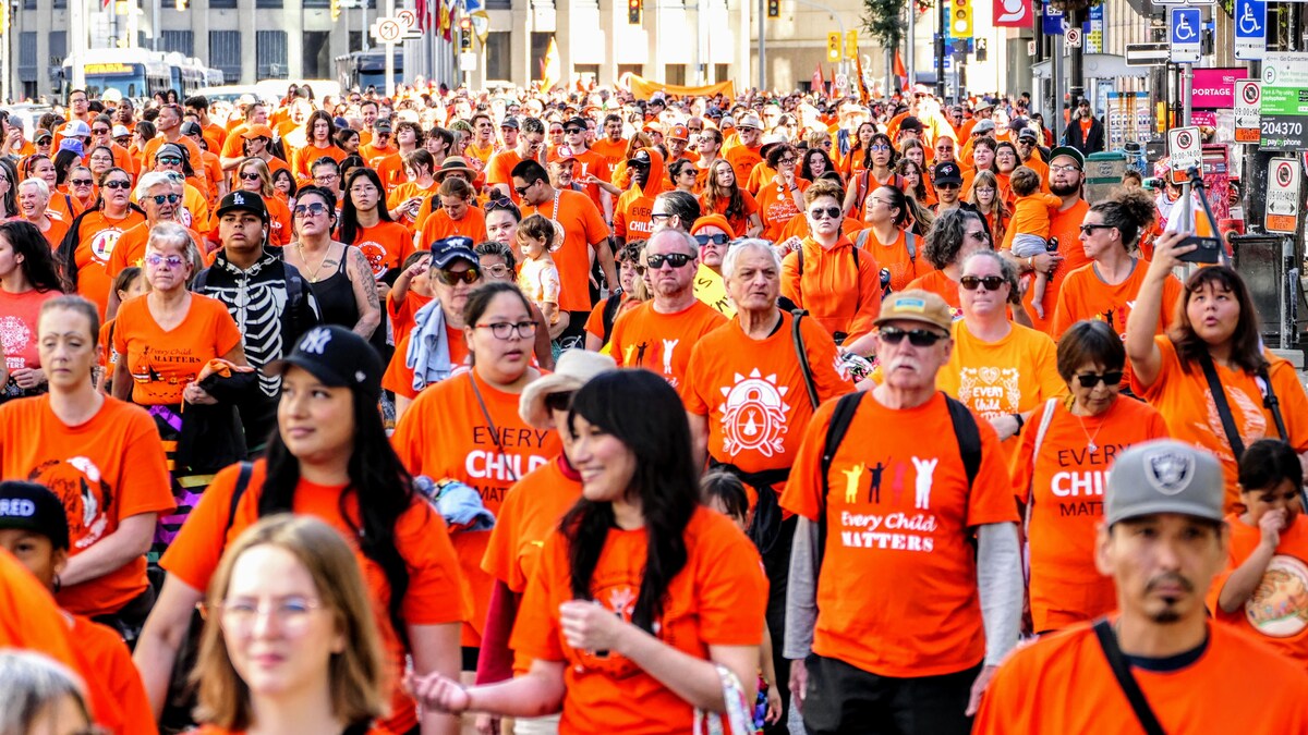 Des centaines de personnes marchent dans les rues du centre-ville de Winnipeg et portent un chandail orange.