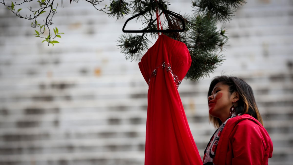 Une personne habillée de rouge a une main rouge peinte sur le visage. Elle est debout près d'une robe rouge accrochée à un arbre.