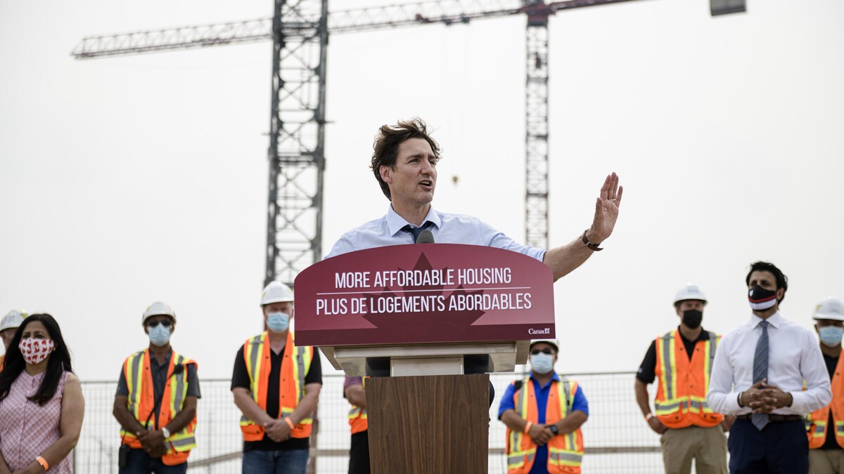 Le premier ministre Justin Trudeau tient un point de presse dans un chantier de construction. On le voit qui parle à un podium avec des travailleurs qui se tiennent derrière lui.