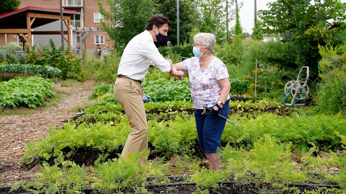 Justin Trudeau salue une femme âgée du coude dans un jardin.