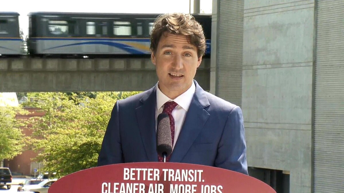 Justin Trudeau devant un Skytrain qui passe.