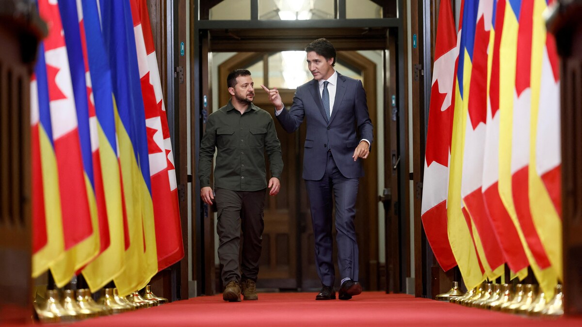 Les deux politiciens marchent entre deux allées de drapeaux canadiens et ukrainiens.
