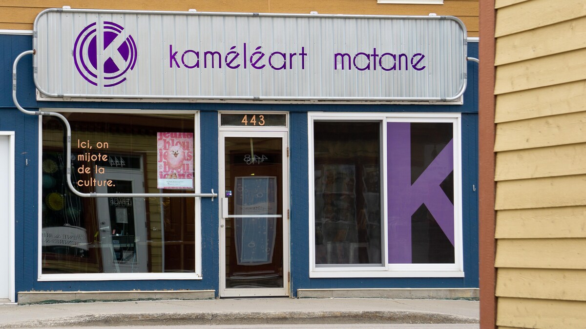Extérieur du bureau. La lettre K est inscrite en grosse lettre dans une vitrine. Sur un panneau publicitaire au-dessus de la porte d'entrée, il est écrit : Kaméléart Matane.