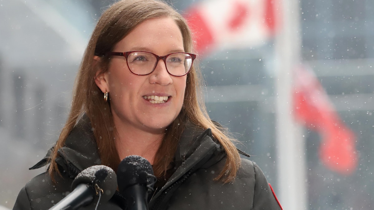 Karina Gould en point de presse à l'extérieur devant un drapeau du Canada.