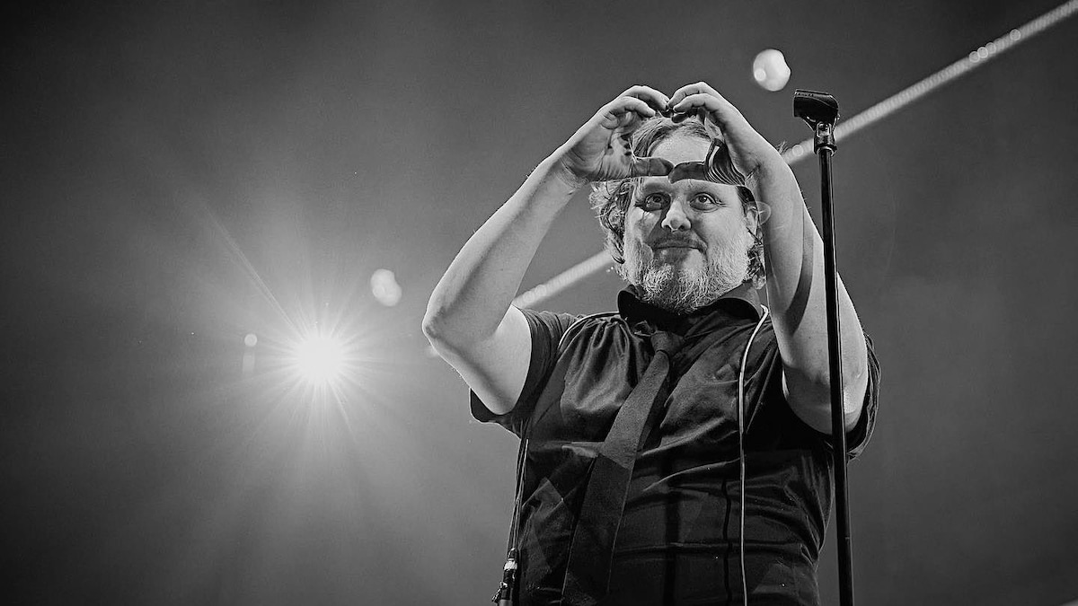 Le chanteur Karl Tremblay fait une forme de cœur avec ses mains sur scène près d'un micro.