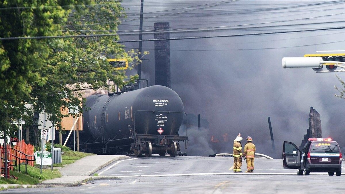 Deux pompiers à côté d'un wagon en plein milieu d'une rue, dans un immense nuage de fumée dense.