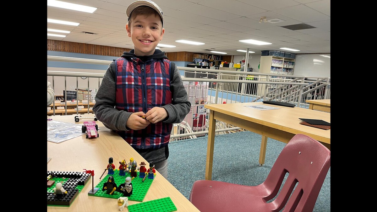 Un jeune garçon est debout à côté d'une table à la bibliothèque devant sa création en Lego.
