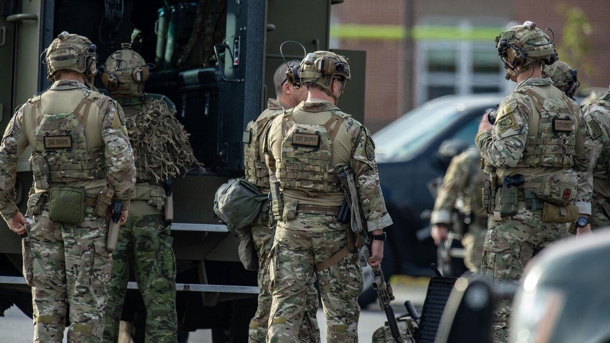 Des policiers en habits de camouflage sont postés près d'un véhicule de police.