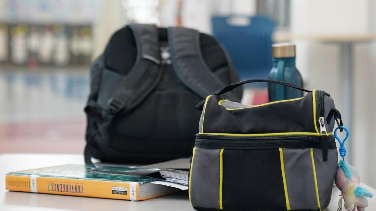 Un sac à lunch, une bouteille d'eau. un sac d'école et un manuel scolaire se trouvent sur une table.