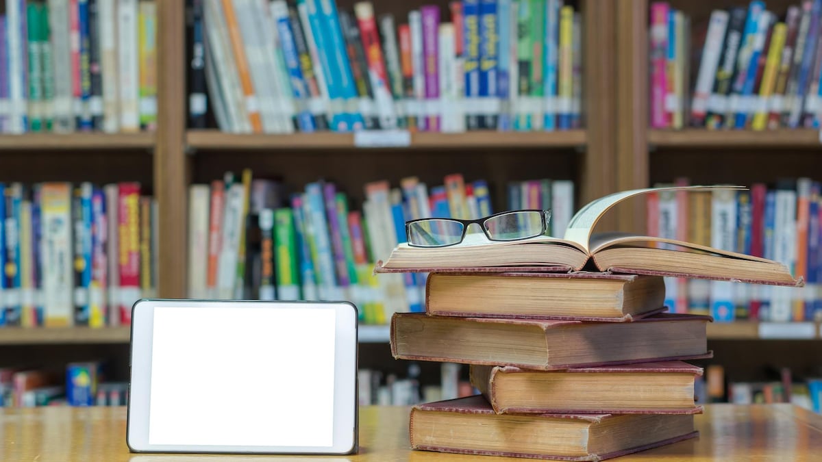 Sur un bureau, des livres sont posés à côté d'une tablette.