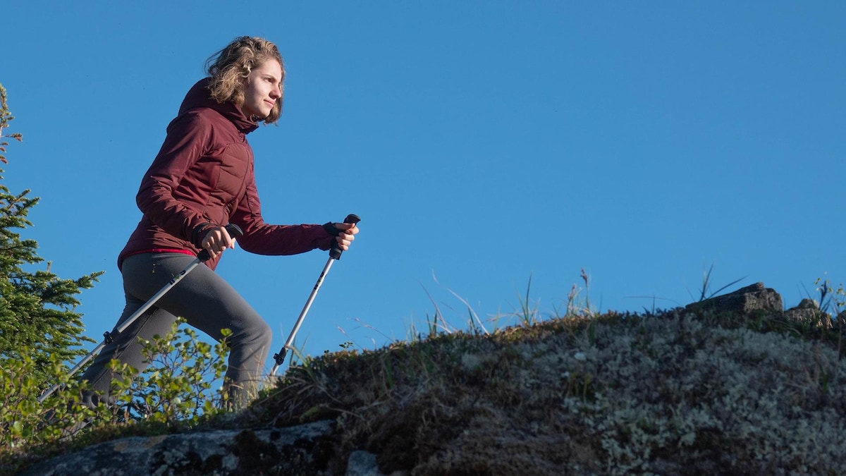 Photographie de Simone, qui marche avec des bâtons de randonnée sur un cap rocheux et montagneux.