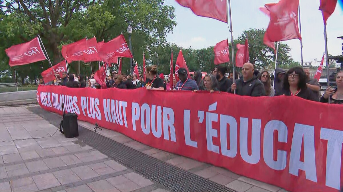 Grande banderole où on peut lire : Viser toujours plus haut pour l'éducation. Derrière, des enseignants qui manifestent debout. 