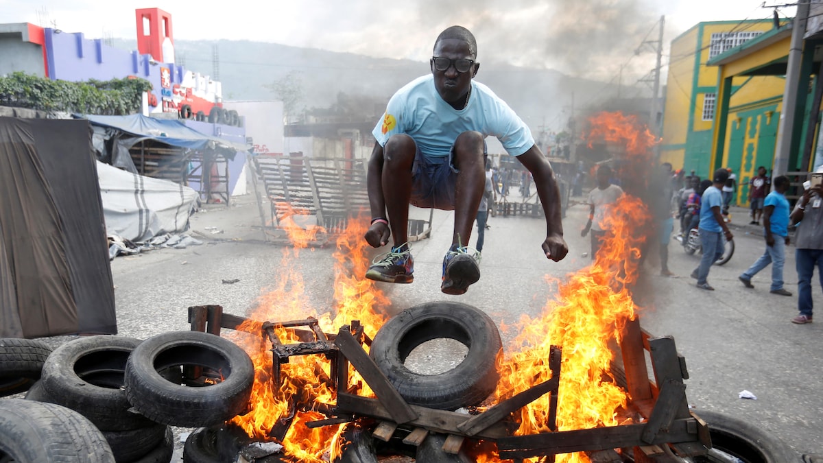 Un homme saute par-dessus des pneus en flammes dans une rue de Port-au-Prince.