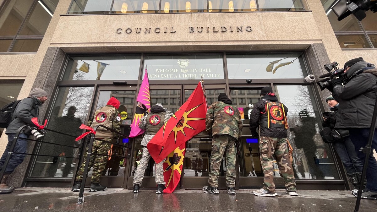Des manifestants ont bloqué les portes de l'hôtel de ville de Winnipeg, vêtus en vêtement d'armée et portant le drapeau des Warriors, le 15 décembre 2022.