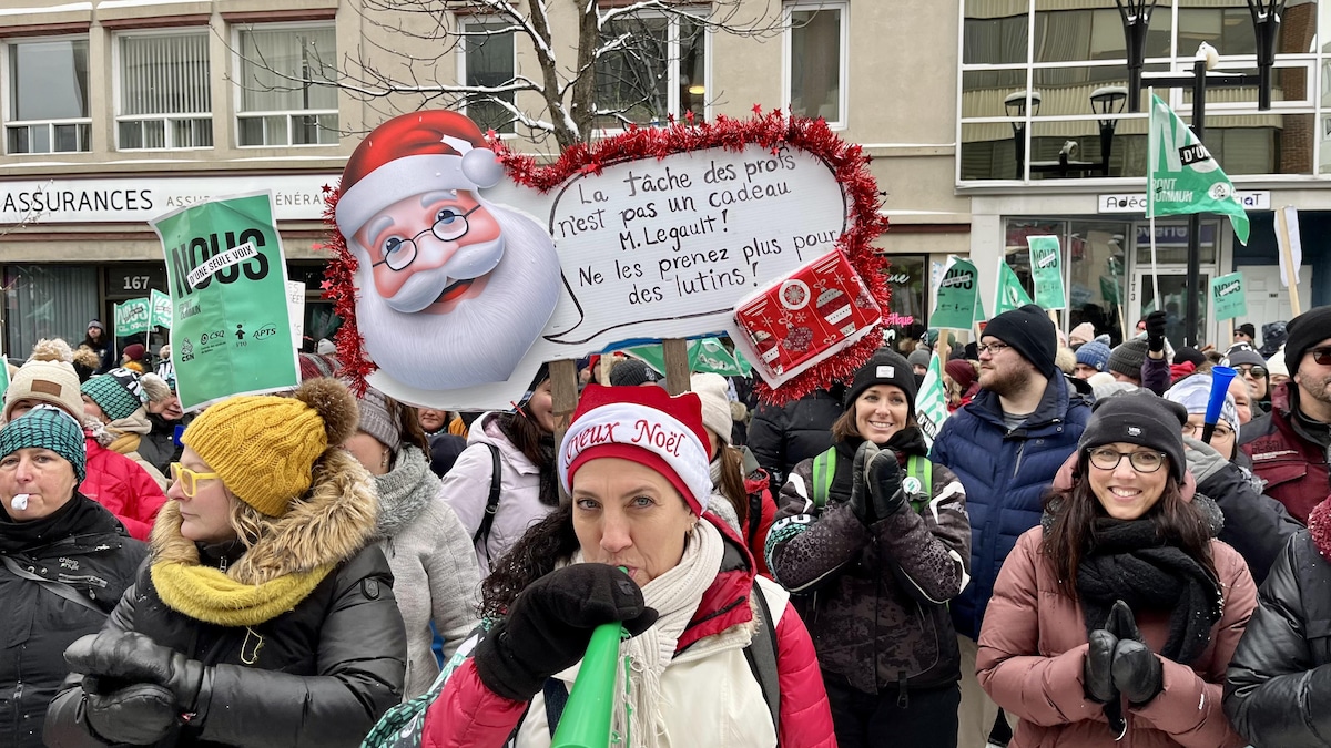 Une manifestante tient une pancarte avec un père Noël qui dit : « La tâche des profs n'est pas un cadeau, monsieur Legault! Ne les prenez plus pour des lutins! »