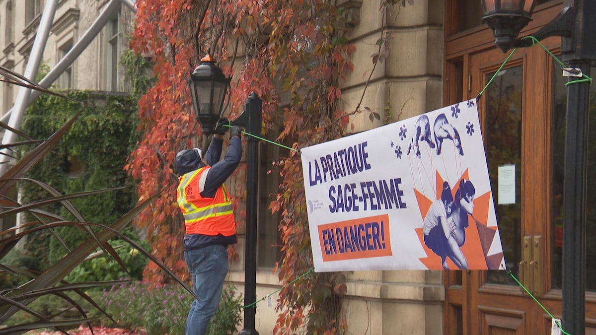 Une personne accroche une banderole qui porte la mention «La pratique sage-femme en danger» bien en vue à Montréal.