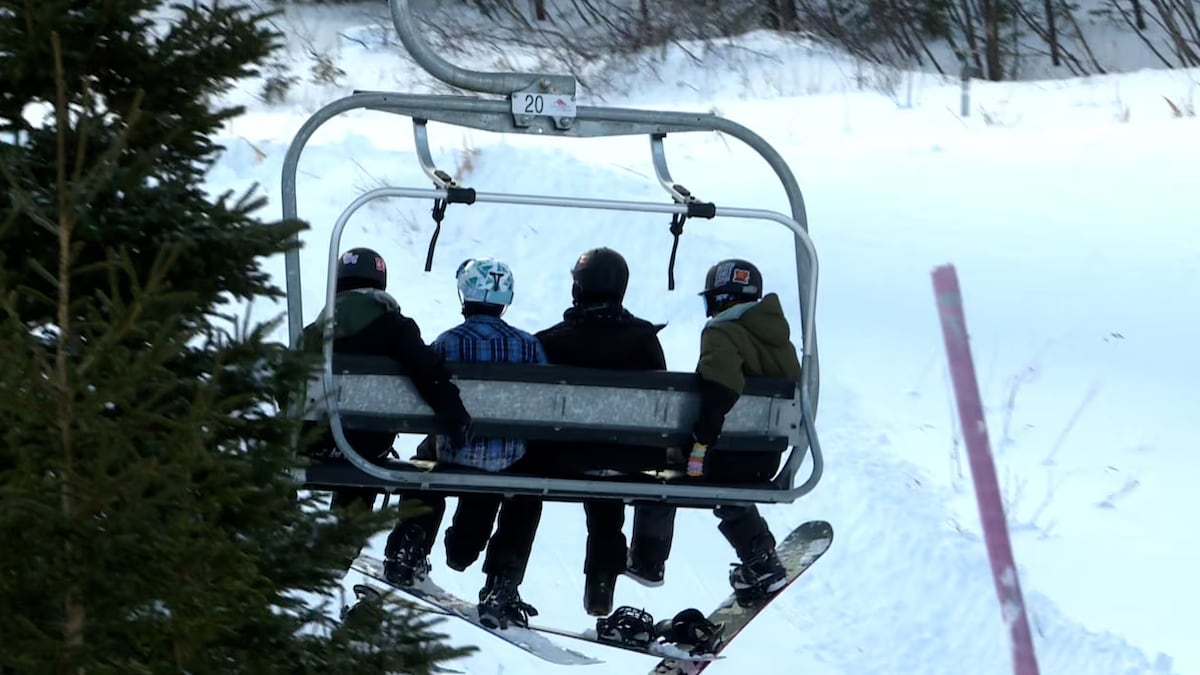 Quatre personnes chaussées de planches à neige sont assises sur un télésiège.
