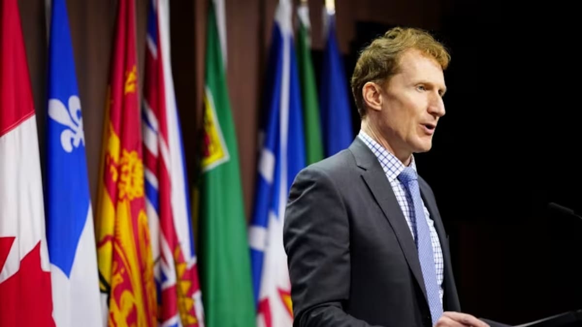 Marc Miller en conférence de presse à Ottawa devant les drapeaux du Canada, des provinces et des territoires.