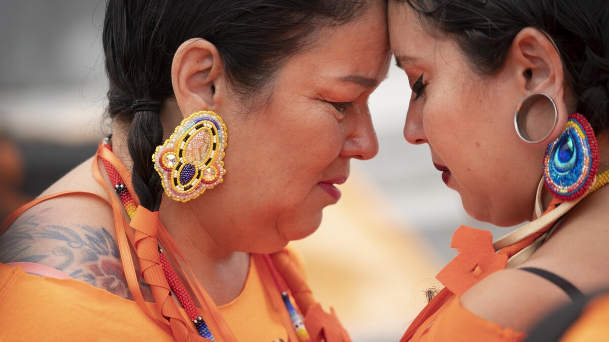 Deux femmes autochtones se serrent, les larmes aux yeux. 