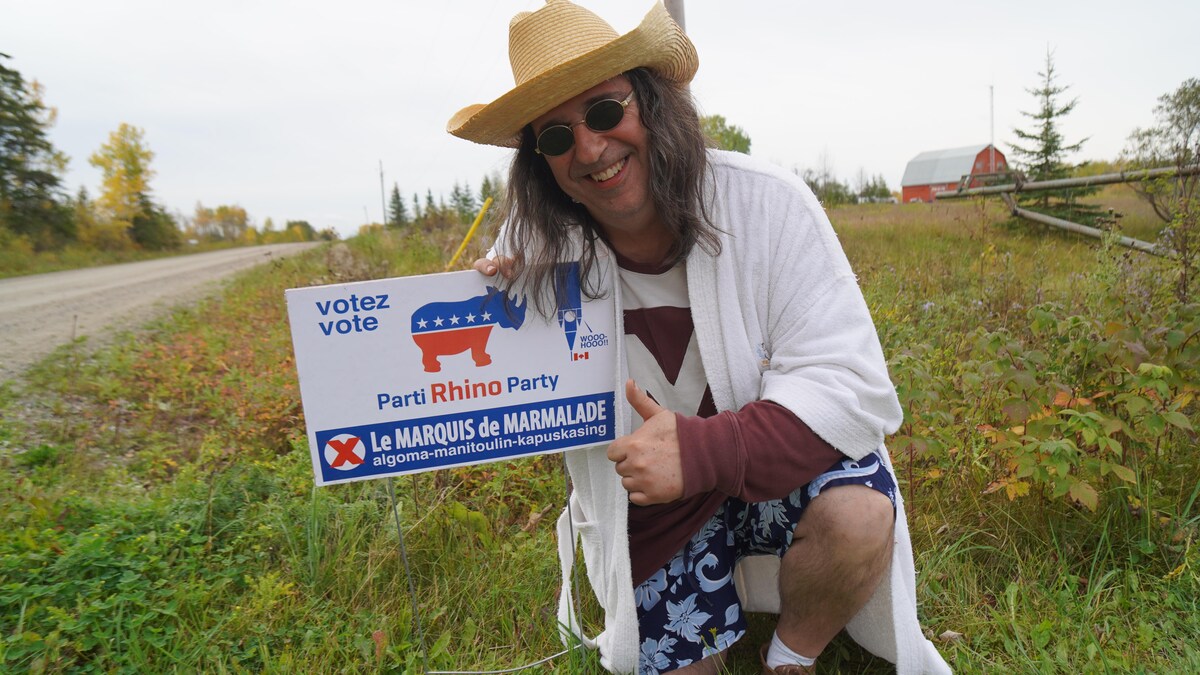 La Marquis de Marmalade sourit devant sa pancarte électorale.