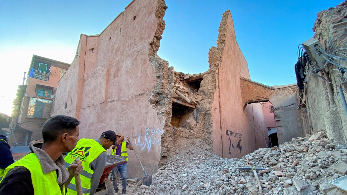 Des secouristes déblaient des décombres devant un mur effondré.