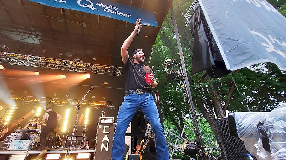 Matt Lang lève son micro dans les airs en souriant à la foule.