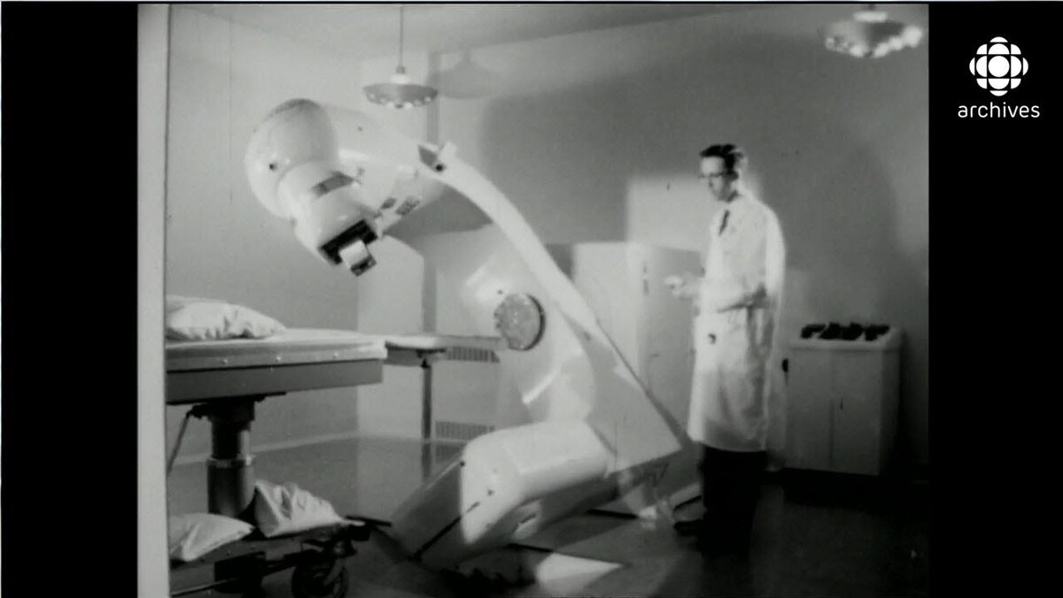 Homme en sarrau manipulant à l'aide d'une manette un gros appareil de médecine nucléaire qui entame une rotation