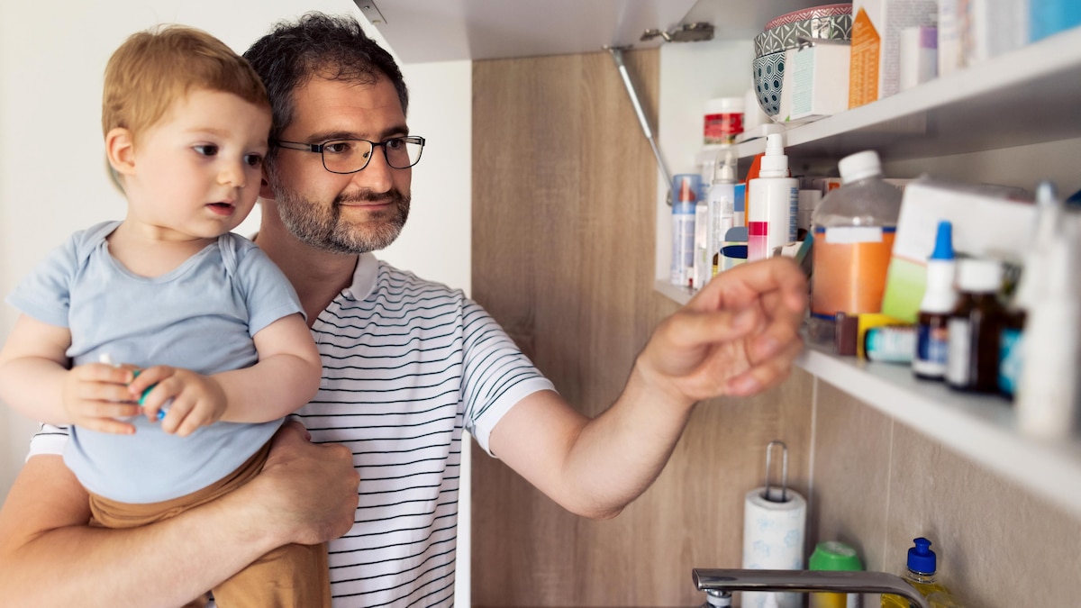 Un père a son enfant dans ses bras et il examine les médicaments dans le cabinet de sa salle de bains.