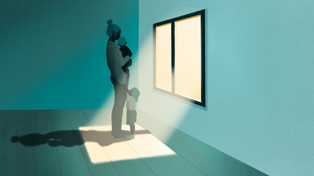 Une mère tenant un enfant dans ses bras regarde par la fenêtre, pendant qu'un autre enfant tire sur son chandail.