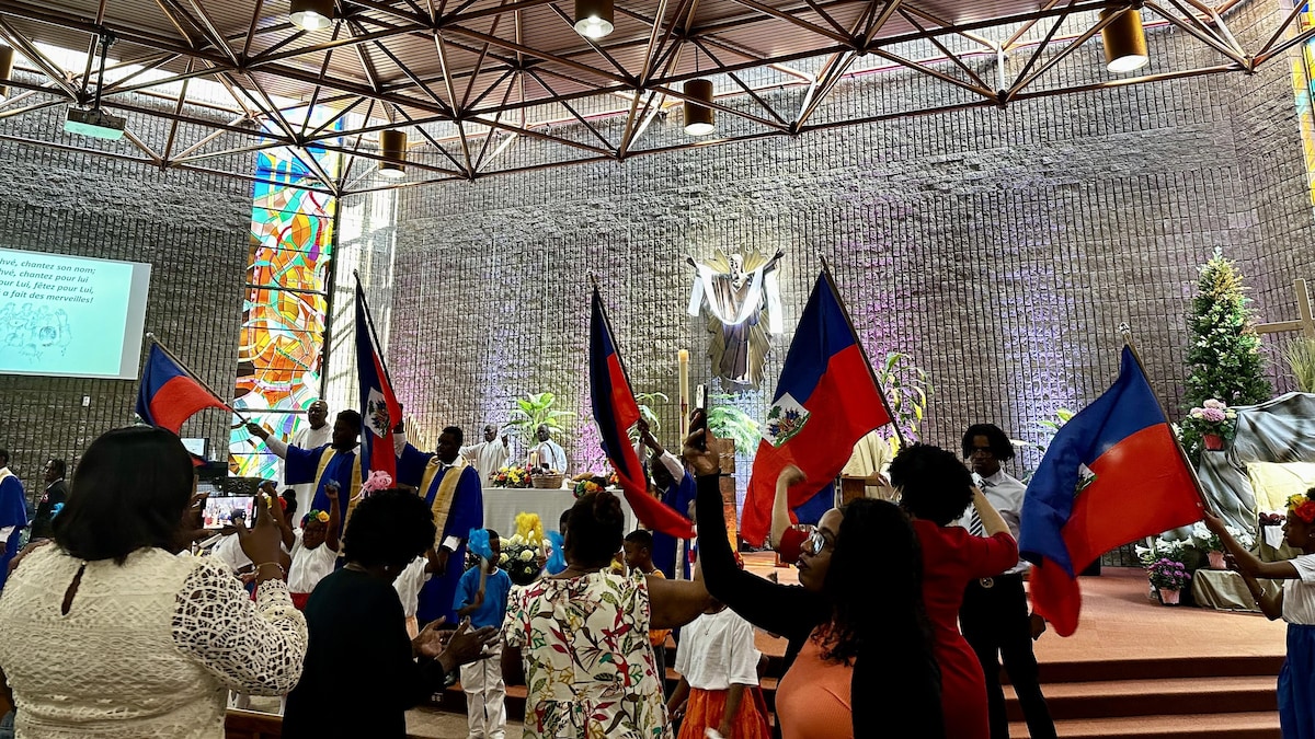 Des personnes brandissent le drapeau d'Haïti dans une église.
