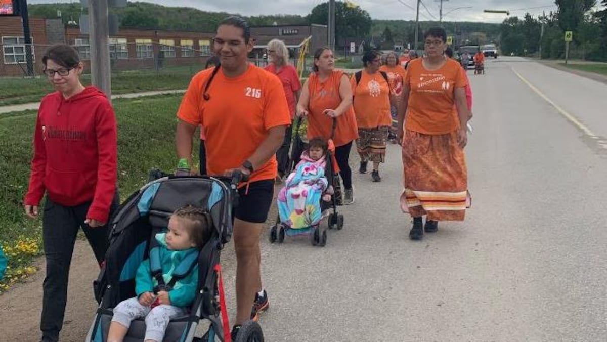 Des Autochtones marchent, vêtus de chandails orange.