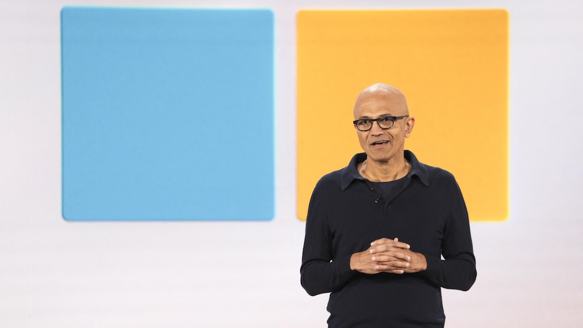 Satya Nadella s'exprime devant un logo de Microsoft.