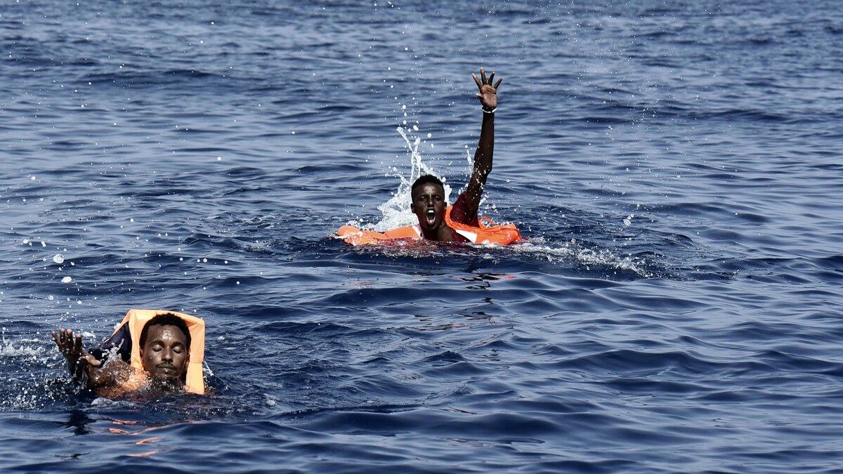 Deux hommes en mer, dont un lève la main en appelant au secours.