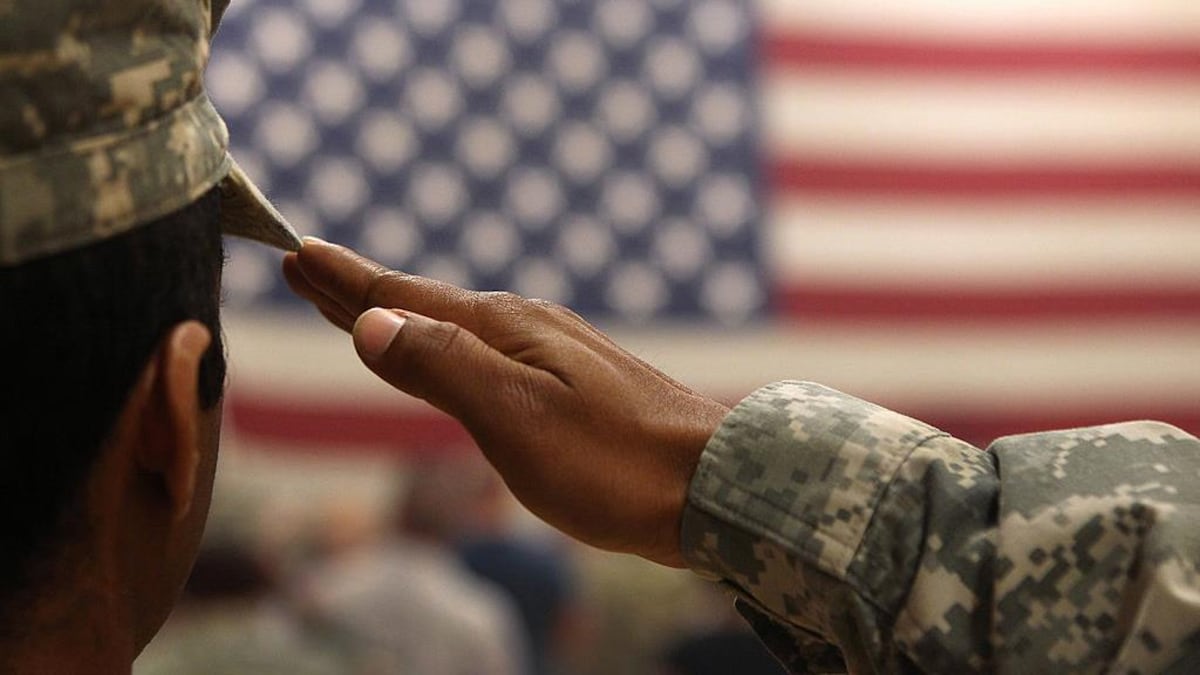 Un homme vêtu d'habits de l'armée fait le salut militaire devant un drapeau des États-Unis.