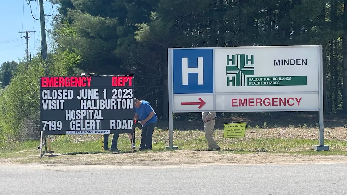 Des ouvriers installent un panneau qui avise les résidents que les urgences locales sont fermées et qu'ils doivent se rendre à Haliburton.