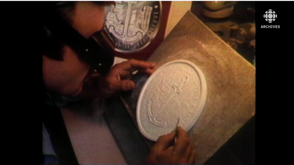 Homme avec lunettes grossissantes qui sculpte dans le plâtre une pièce représentant une ancre de bateau. 