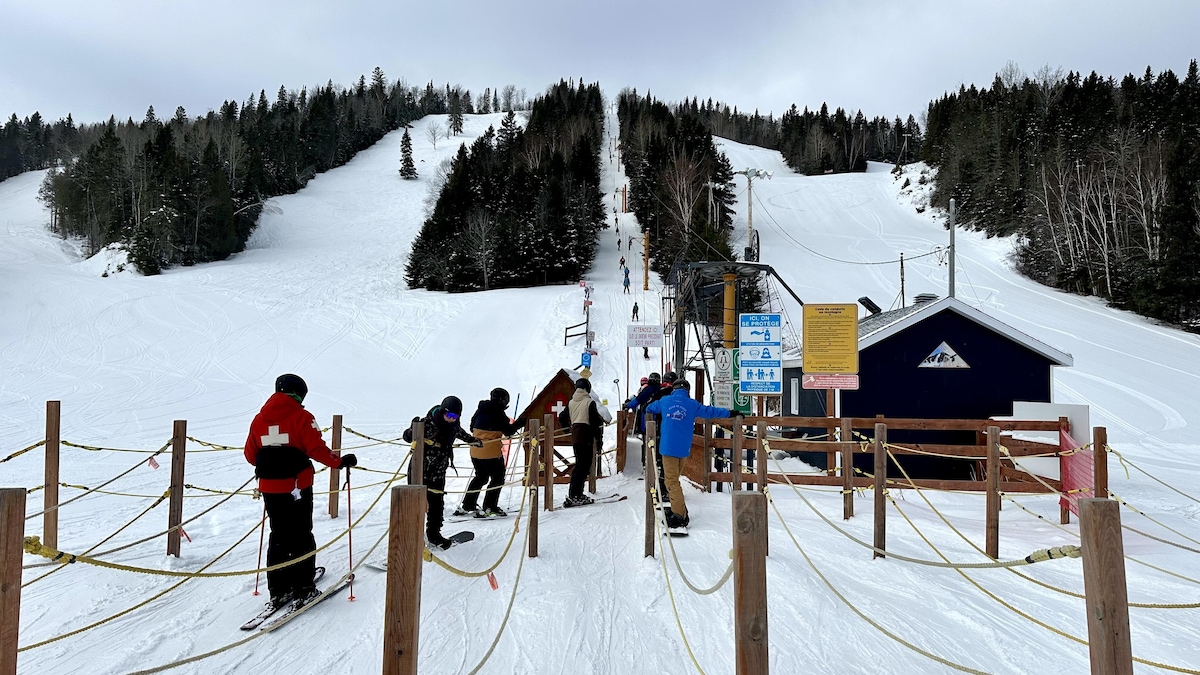 Des skieurs et des planchistes font la queue pour la remontée mécanique au pieds des pistes de ski alpin enneigés du Mont-Castor.