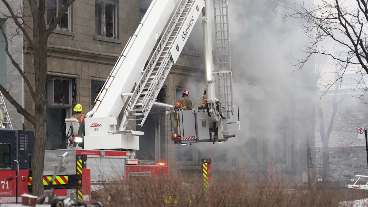 Les pompiers arrosent la façade d'un immeuble d'où s'échappe une épaisse fumée.