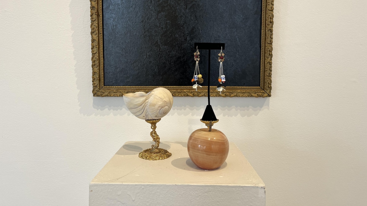 Un coquillage, des bijoux et une pomme devant un cadre. 