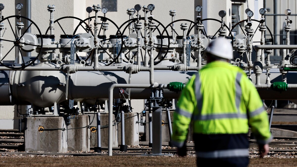 Un ouvrier marche près de valves et de toyaux à L'extérieur.