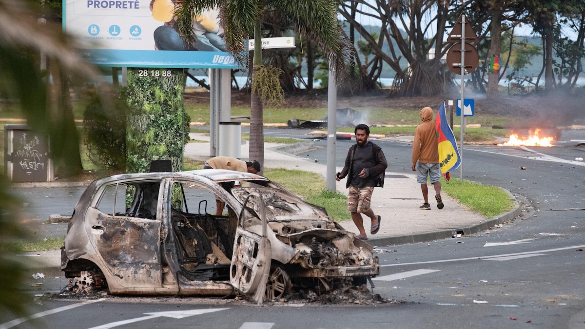 Des personnes marchent à côté d'une voiture incendiée.