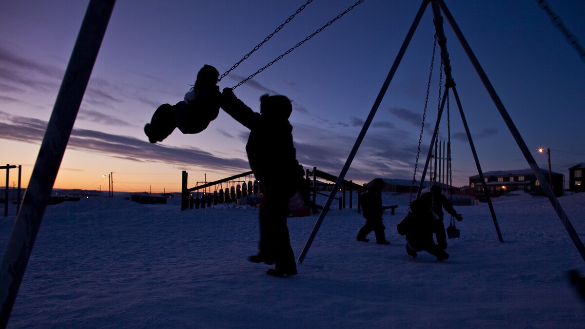 Un adulte pousse un enfant sur une balançoire tandis que d'autres enfants jouent à côté d'eux, à Iqaluit, au Nunavut, le 4 février 2009. 