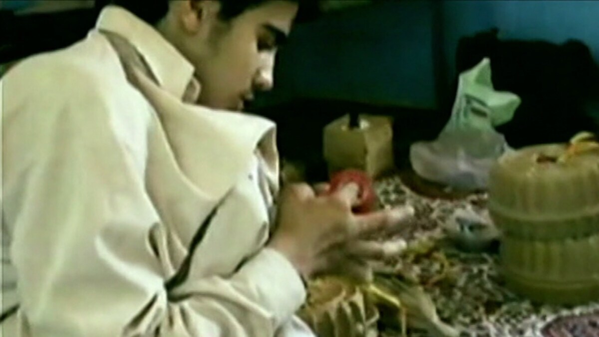 Omar Khadr, enfant, agenouillé sur un tapis, affairé à dérouler du ruban adhésif.