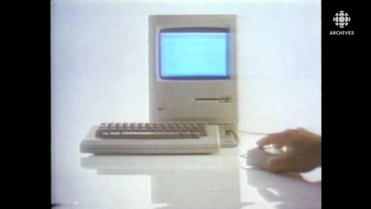 Écran et clavier du nouvel ordineur de Macintosh en 1984. Une main est posée sur la souris.