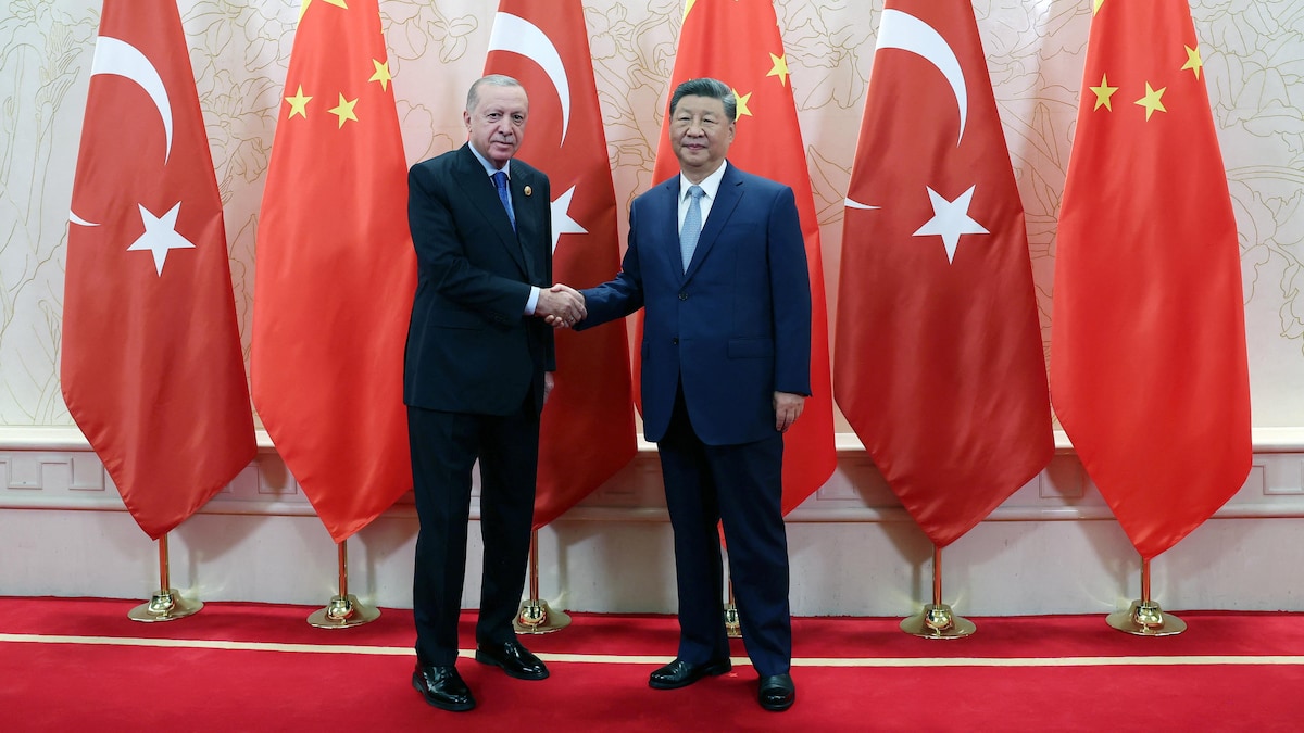 Tayyip Erdogan et Xi Jinping se serrent la main devant des drapeaux de la Turquie et de la Chine.