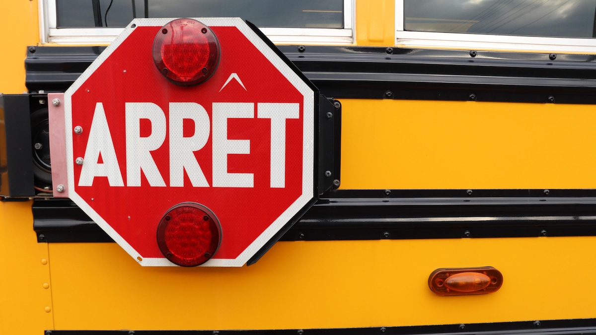 Un panneau d'arrêt avec deux feux clignotants rouge sur le côté d'un autobus scolaire.