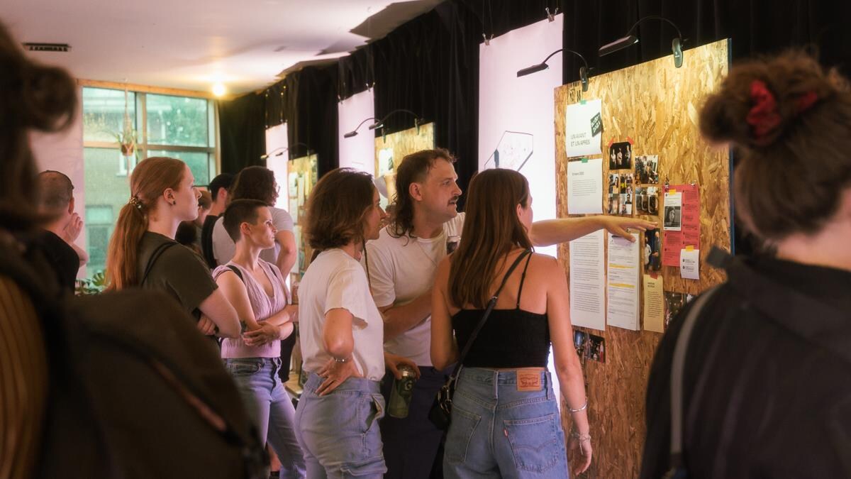 Des jeunes regardent des archives au mur. Un homme pointe du doigt une affiche. 