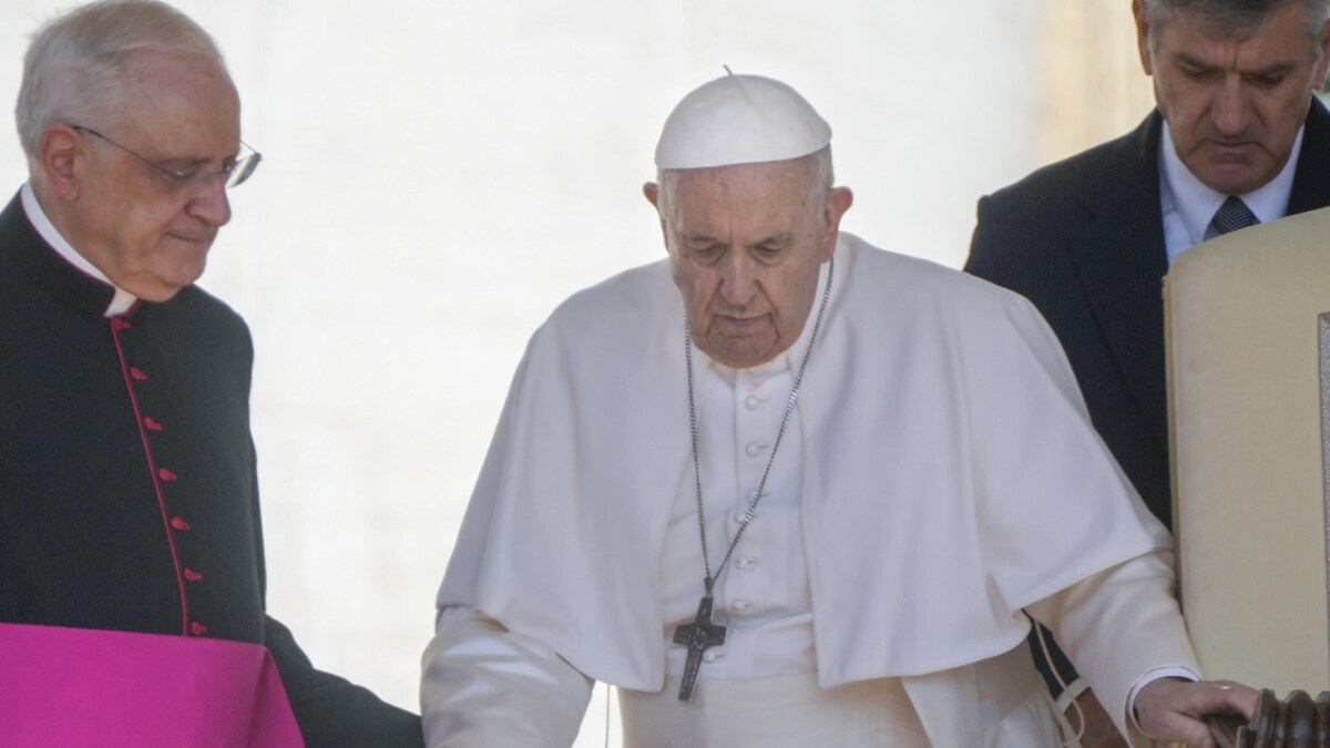 Le pape muni d'une canne est aidé par un cardinal.