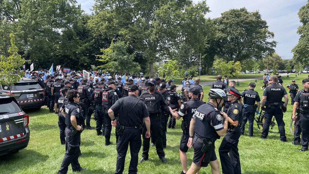 Des dizaines de policiers restent aux aguets. Au loin, on voit des dizaines de manifestants avec des affiches.