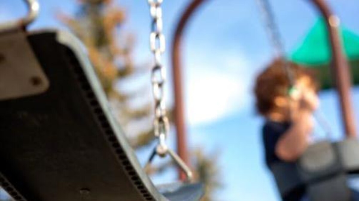 Une balançoire dans un parc et un enfant sur une structure de jeu. La photo est floue. 